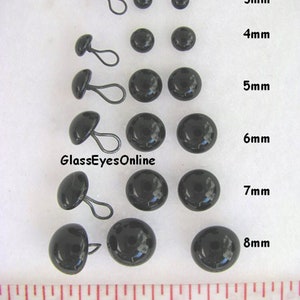 May include: Assortment of black glass eyes with wire loops in various sizes, ranging from 3mm to 8mm. A ruler is included for size reference. #LP201 Glass Eyes with Wire Loops - Black