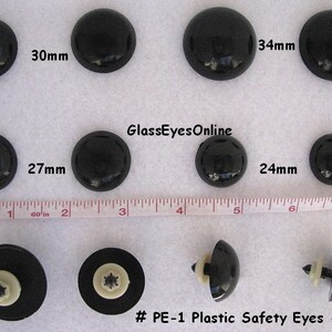 May include: Assortment of black plastic safety eyes in various sizes, ranging from 24mm to 34mm. The eyes are labelled with their size in millimetres. The text "#PE-1 Plastic Safety Eyes - Black" is displayed at the bottom of the image.