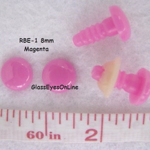 K&ouml;nnte beinhalten: Vier rosafarbene Kunststoff-Sicherheitsaugen mit Schraubverschluss. Die Augen haben einen Durchmesser von 8 mm und sind neben einem Lineal abgebildet. Der Text "RBE-1 8mm Magenta" ist im Bild sichtbar.