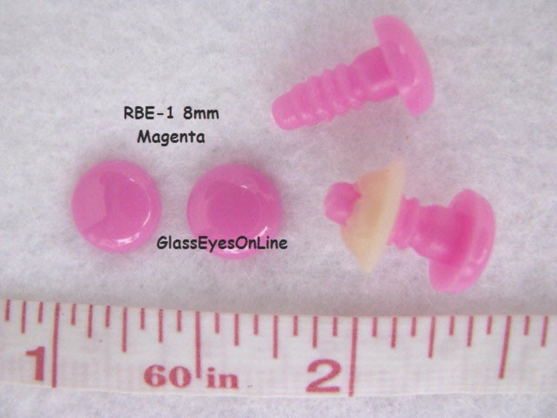 K&ouml;nnte beinhalten: Vier rosafarbene Kunststoff-Sicherheitsaugen mit Schraubverschluss. Die Augen haben einen Durchmesser von 8 mm und sind neben einem Lineal abgebildet. Der Text "RBE-1 8mm Magenta" ist im Bild sichtbar.