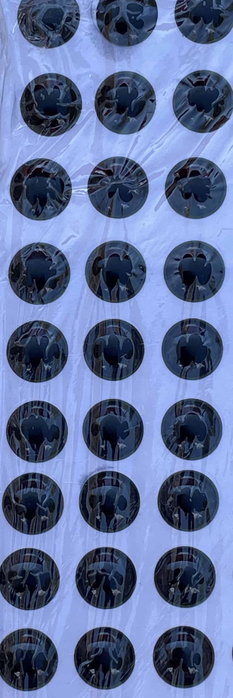 May include: A sheet of black and gray round stickers with a clover design. The stickers are arranged in rows on a white background.