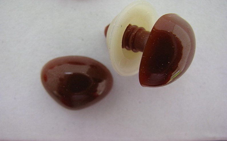 May include: Two brown plastic safety eyes for crafts. One eye is attached to a white plastic washer. The eyes are glossy and have a slight sheen.