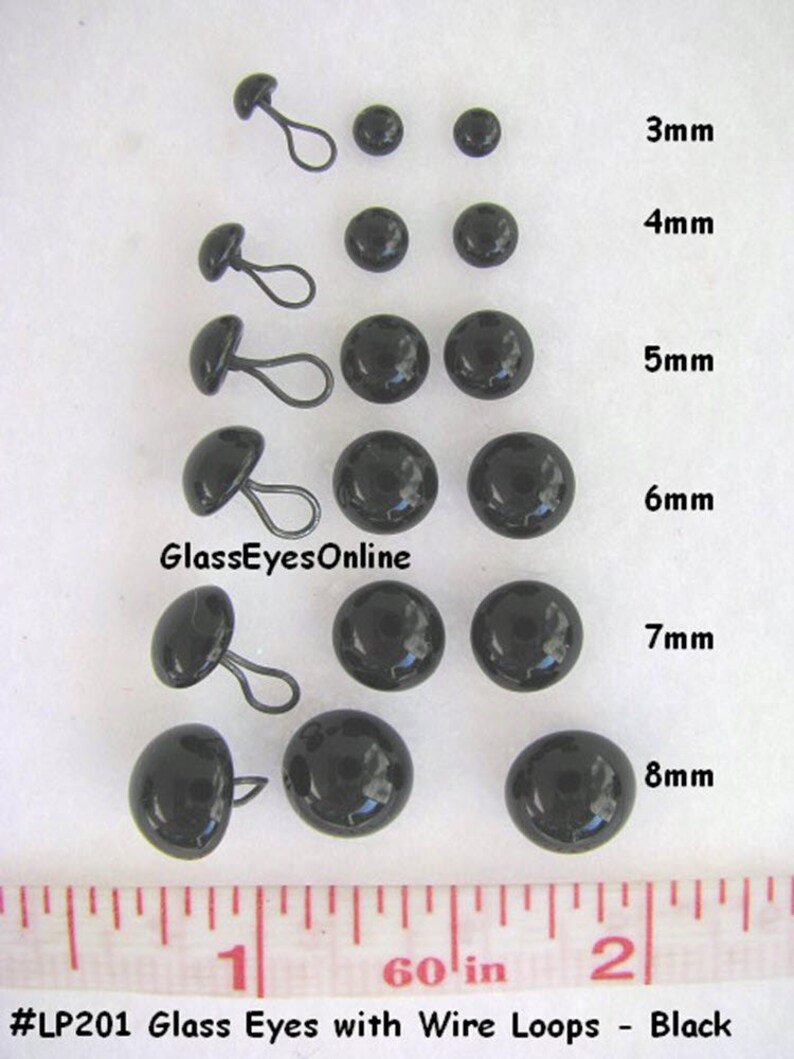 May include: Assortment of black glass eyes with wire loops in various sizes, ranging from 3mm to 8mm. A ruler is included for size reference. #LP201 Glass Eyes with Wire Loops - Black