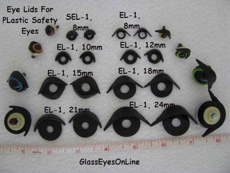 May include: Assortment of black plastic eye lids for plastic safety eyes in various sizes, ranging from 8mm to 24mm. The eye lids are arranged on a white surface with a ruler for size reference. The text "SEL-1, 8mm" and "EL-1, 8mm" are visible in the image.