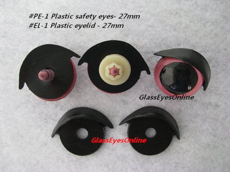 May include: Four plastic safety eyes and eyelids for crafts. Two black plastic safety eyes with pink eyelids and two black plastic eyelids. The eyes are 27 mm in diameter. The text on the image reads "#PE-1 Plastic safety eyes - 27mm #EL-1 Plastic eyelid - 27mm GlassEyesOnline".