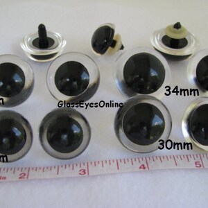 May include: Assortment of clear plastic safety eyes with black pupils in various sizes, including 24mm, 27mm, 30mm, and 34mm.  GlassEyesOnline is printed on the image.
