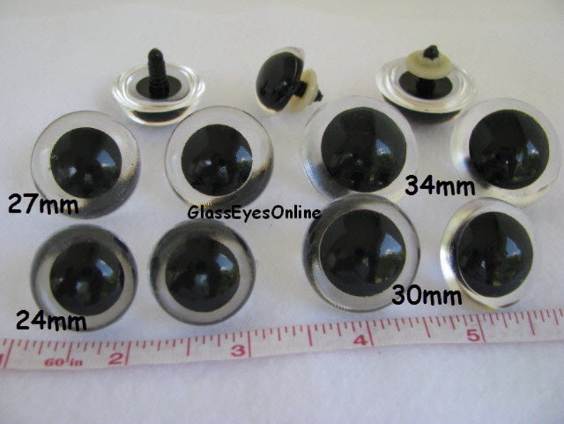 May include: Assortment of clear plastic safety eyes with black pupils in various sizes, including 24mm, 27mm, 30mm, and 34mm.  GlassEyesOnline is printed on the image.