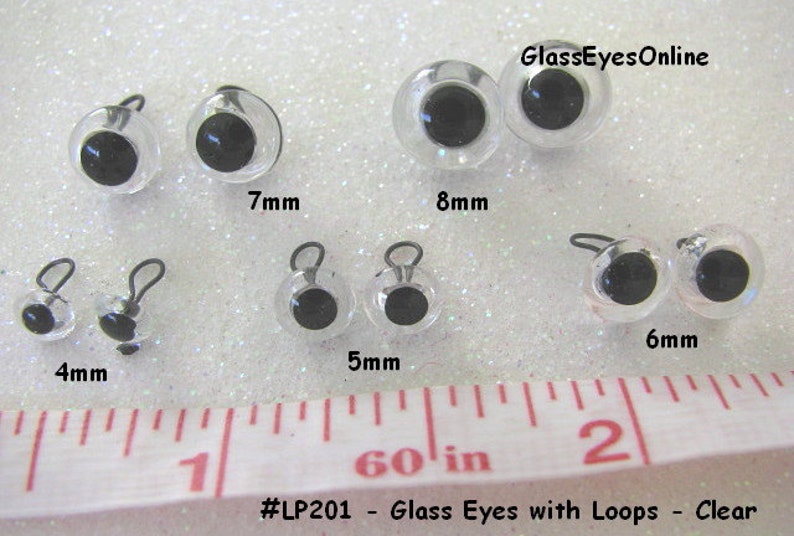 May include: Assortment of clear glass eyes with black pupils and metal loops. The eyes are arranged in rows by size, with measurements in millimeters. The text "#LP201 - Glass Eyes with Loops - Clear" and "GlassEyesOnline" are visible in the image.