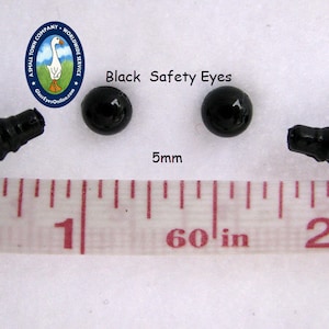 May include: Two black plastic safety eyes with a screw back, measuring 5mm in diameter. The eyes are shown next to a ruler with the measurement 5mm marked.