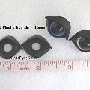 May include: Four black plastic eyelids for doll making. Two eyelids are closed and two are open with black and white eyes. The eyelids are 15mm in size. A ruler is in the background for size reference.