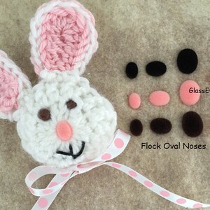 May include: White crocheted bunny with pink ears and a pink polka dot ribbon. The bunny has brown eyes and a pink felt nose. The image also shows a variety of black and brown felt eyes and noses.