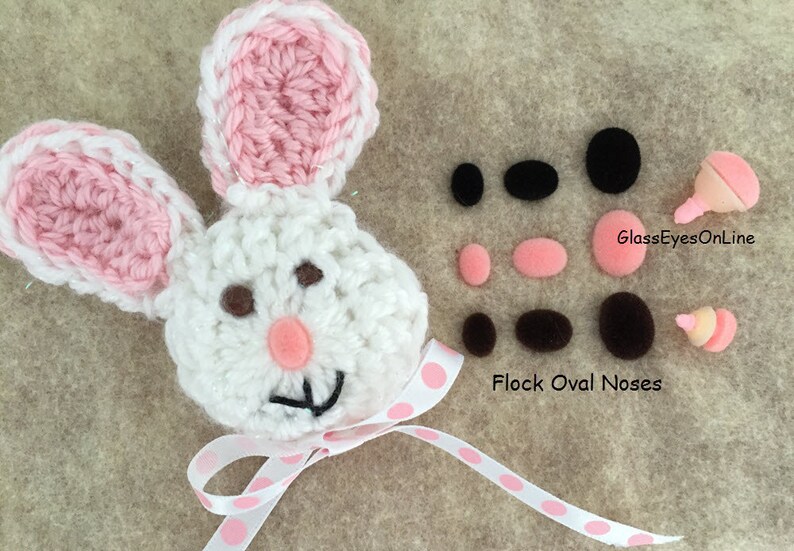 May include: White crocheted bunny with pink ears and a pink polka dot ribbon. The bunny has brown eyes and a pink felt nose. The image also shows a variety of black and brown felt eyes and noses.