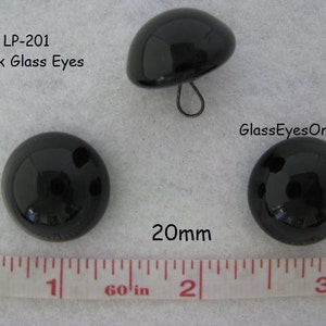 May include: Two black glass eyes, each measuring 20mm in diameter. The eyes are round and have a shiny, reflective surface. The text "LP-201 Black Glass Eyes" and "GlassEyesOnLine" are visible in the image.