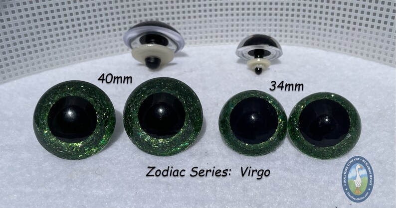 May include: Two pairs of green glitter safety eyes for stuffed animals. The larger pair is 40mm and the smaller pair is 34mm. The eyes have black pupils and a green glitter finish. The text "Zodiac Series: Virgo" is printed below the eyes.