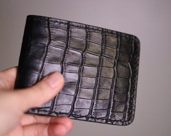 May include: A black leather wallet with a crocodile embossed pattern.
