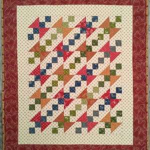 May include: Handmade quilt featuring a repeating pattern of colorful triangles and squares in red, blue, green, and orange. The quilt has a cream-colored background with a patterned border in a deep red hue.