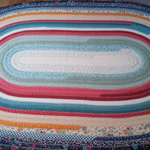 May include: A colorful oval braided rug with a white center and multiple bands of red, blue, yellow, and green fabric.