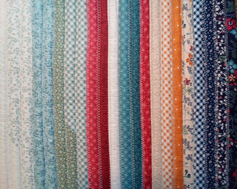May include: A close-up of a fabric strip quilt with various patterns and colors, including white, blue, green, red, orange, and brown.