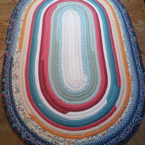 May include: A colorful oval braided rug with a variety of floral and geometric patterns in shades of blue, red, orange, and white.