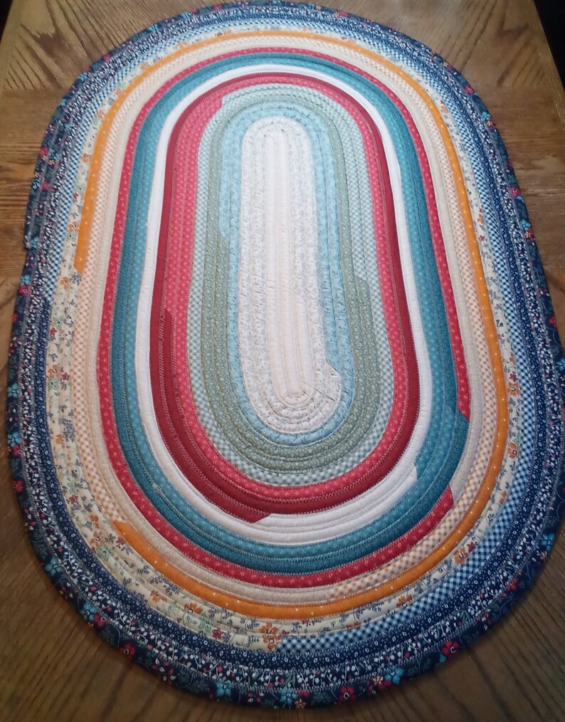 May include: A colorful oval braided rug with a variety of floral and geometric patterns in shades of blue, red, orange, and white.