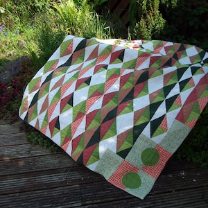 May include: A patchwork quilt with a geometric pattern of green, red, and white triangles. The quilt is made of different fabrics and has a rustic, handmade look.