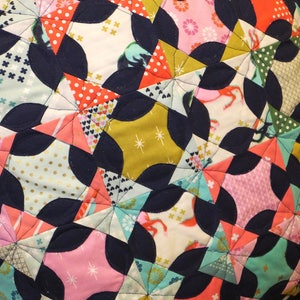 May include: A navy blue, pink, green, and gold patchwork quilt with a geometric pattern. The quilt is made of various fabrics with different patterns and textures.