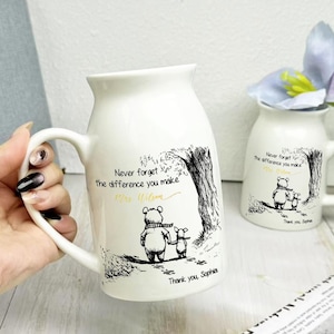 Peut inclure: Mug en céramique blanche avec une illustration en noir et blanc d'un ours et d'un porcelet sous un arbre. Le mug porte l'inscription "N'oubliez jamais la différence que vous faites" et "Merci, Sophia."