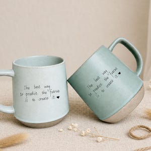 Può includere: Due tazze in ceramica azzurro chiaro con finitura maculata e base liscia non smaltata. Ogni tazza presenta il testo stampato in nero: The best way to predict the future is to create it, seguito da un piccolo simbolo di cuore nero sul lato.