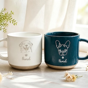 Puede incluir: Dos tazas de cerámica con acabado liso y base natural. La taza blanca presenta una ilustración de líneas de un golden retriever y el nombre Peanut. La taza azul cerceta presenta una ilustración de líneas de un bulldog francés y el nombre Peanut.