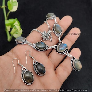 Könnte beinhalten: Ein silberfarbenes Halsketten- und Ohrring-Set mit ovalen, schillernden Edelsteinen. Die Halskette hat eine Kette und mehrere Edelsteinanhänger. Die Ohrringe haben ein Haken-Design. Das Wasserzeichen The Purified Gems ist sichtbar.