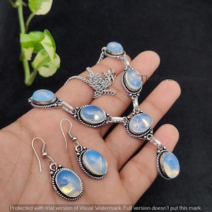 May include: A silver necklace and earring set featuring oval opalescent gemstones. The necklace has a chain and multiple gemstone pendants. The earrings have a hook design. The gemstones are set in a decorative silver frame.