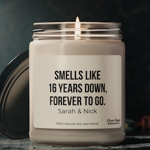 A white candle jar with a black lid stands on a white surface. The label on the jar reads, Smells Like 16 Years Down, Forever to Go. The candle brand Clever Flames and it makes a perfect personalized gift a 16th anniversary.