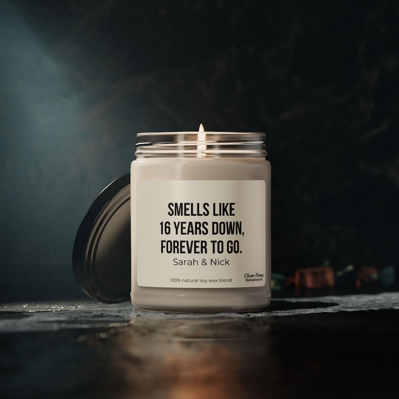 A white candle jar with a black lid stands on a white surface. The label on the jar reads, Smells Like 16 Years Down, Forever to Go. The candle brand Clever Flames and it makes a perfect personalized gift a 16th anniversary.
