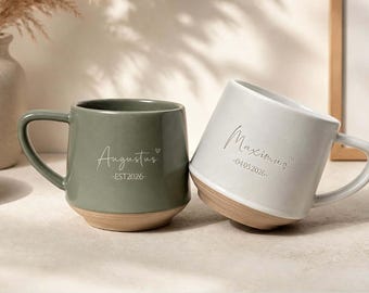 May include: Two ceramic mugs with a handle and a natural clay base. The sage green mug features the text Augustus and EST 2026. The off-white mug features the text Maximus and 04.05.2026. Both mugs include a small heart icon next to the name.