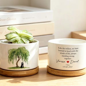 May include: Two white ceramic cylindrical planters on round bamboo bases. One planter holds a green succulent and features a watercolor willow tree with a couple underneath. The other displays the text: Like the willow, we have learned to bend with the winds of life, always standing strong together. Vanessa, a red heart, Daniel, 9 Years, 13.08.2017.