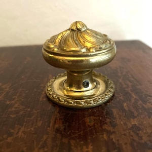 May include: A vintage brass doorknob with an ornate, floral design. The knob has a rounded top and a decorative base with a detailed edge. The brass has a warm, aged patina, suggesting its antique nature. The doorknob is a classic piece of hardware.