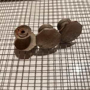 May include: Three antique metal cabinet knobs with a weathered appearance. The knobs have a hexagonal shape and are likely made of steel or a similar metal. They are arranged on a wire mesh surface.