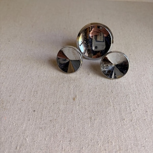 May include: Three circular, metallic cabinet knobs with a polished chrome finish. The knobs feature a conical, faceted center design that reflects light, creating a star-like pattern. The largest knob is positioned behind two smaller, identical knobs.