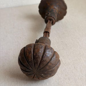 May include: A dark brown, rusted metal door knob with a fluted, pumpkin-like shape. The knob features a central spindle connecting to a matching circular backplate. The surface shows significant oxidation and a textured, weathered appearance.