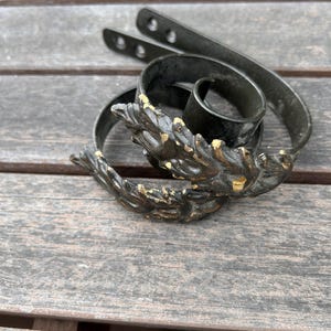 May include: A pair of dark metal decorative candle holders with a leaf design and gold accents. The candle holders are curled and have a rustic appearance. The background is a wooden surface.