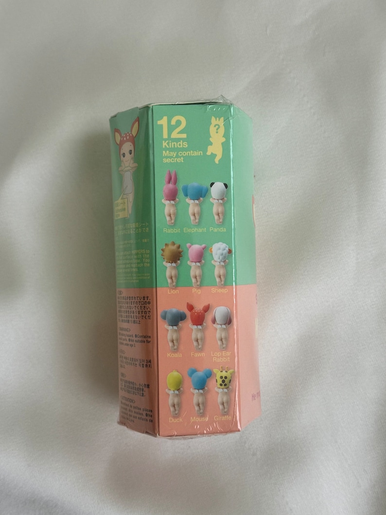 May include: A sealed, hexagonal box in green and pink. The box displays illustrations of small figurines with animal-themed hats. Text on the box reads "12 Kinds May contain secret" and lists animal names such as Rabbit, Elephant, and Panda.