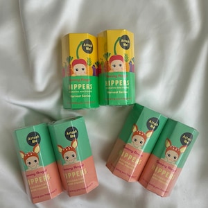 May include: A collection of Sonny Angel Harvest Series decorative mini figures are shown. The packaging is in shades of yellow, green, and peach, featuring a baby with a vegetable-themed hat. The text "Attach Me!" is visible on the boxes.