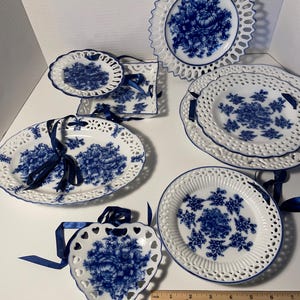 May include: Set of seven blue and white porcelain plates with intricate lace designs. The plates feature floral patterns and are decorated with blue ribbons.