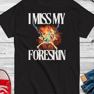 May include: Black t-shirt with a white graphic of a skeleton holding two guns with an explosion behind it. The text "I Miss My Foreskin" is printed in white above the graphic.