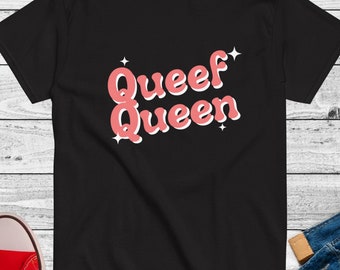 Puede incluir: Camiseta negra con un gráfico rosa que dice "Queef Queen" con estrellas a cada lado.