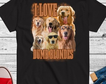 Puede incluir: Camiseta negra con un gráfico de seis golden retrievers y el texto "I LOVE DUMB BLONDES" en marrón. Algunos perros llevan gafas de sol y gafas. La camiseta se muestra sobre una superficie de madera blanca.