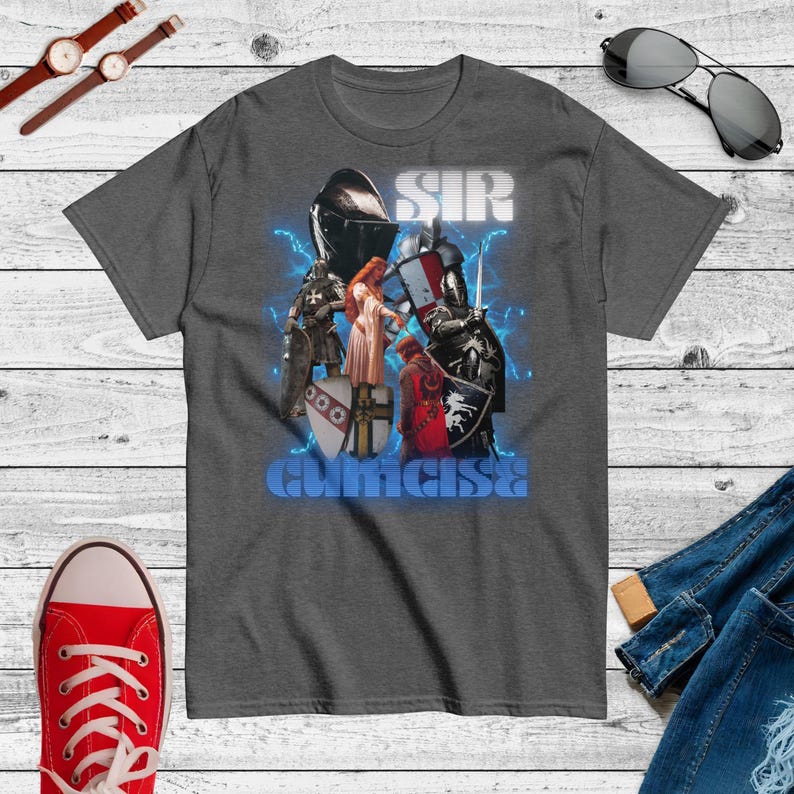 May include: Charcoal grey t-shirt with a graphic design of knights, a woman, and the words "SIR" and "CURICISE" in blue and white. The design includes lightning bolt accents and medieval imagery.