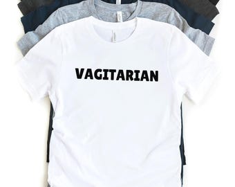 Puede incluir: Camiseta blanca con el texto "VAGITARIAN" impreso en negro.