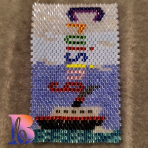 Könnte beinhalten: Ein Perlenbild eines roten Bootes mit einem weiß-rot gestreiften Segel, einem gelben Mast und einer Regenbogenflagge. Das Boot befindet sich auf einem blauen Hintergrund mit weißen Wellen.