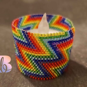 May include: A rainbow beaded candle holder with a white tea light inside. The holder is made of small, colorful beads that are woven together in a pattern.